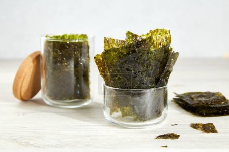 Algues nori croustillantes dans des bocaux en verre sur fond gris. Feuilles traditionnelles japonaises d'algues sèches. Une collation saine