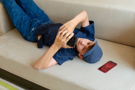 Photo for Teenager boy relax sit on sofa at home using cellphone texting chatting with friend, shop online or check mobile application or social media. Smartphone and surfing the internet. - Royalty Free Image