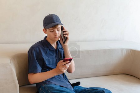 Photo for Teenager boy relax sit on sofa at home using cellphone texting chatting with friend, shop online or check mobile application or social media. Smartphone and surfing the internet. - Royalty Free Image
