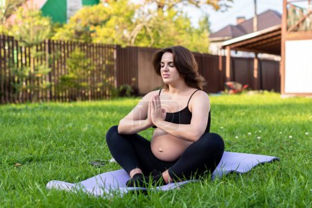 Photo for Pregnant woman doing yoga and meditating on grass in the yard, deep breath with fresh air do yoga lotus pose comfortable. Yoga Motherhood, mental health, and Pregnant Concept. - Royalty Free Image