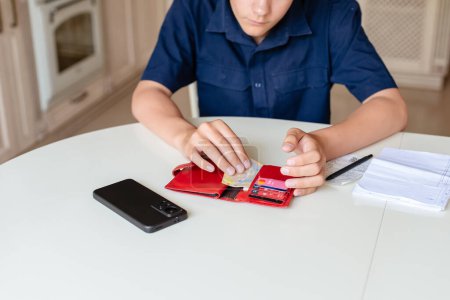 Photo for Teen boy is counting checking the pocket money in his wallet, home background. Freelancer, work for students, first salary. Money saving, self finance, planning. - Royalty Free Image