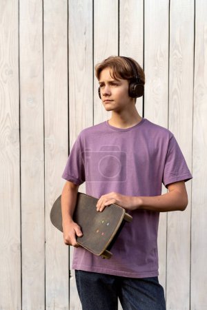 Photo for Teen boy with headphones holding langboard outdoor on white background. Child spending free time relaxing, listening music. Technology, teen hobby, lifestyle and people concept - Royalty Free Image