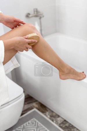 Photo for Woman holding wooden brush and doing dry massage on her body. Self care concept. Beauty spa massage skin and body scrub, cosmetology, peeling, spa cosmetic - Royalty Free Image
