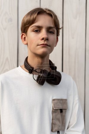 Photo for Portrait of teen boy with headphones outdoor on wooden white background. Child spending free time relaxing. Technology, lifestyle and people concept. - Royalty Free Image