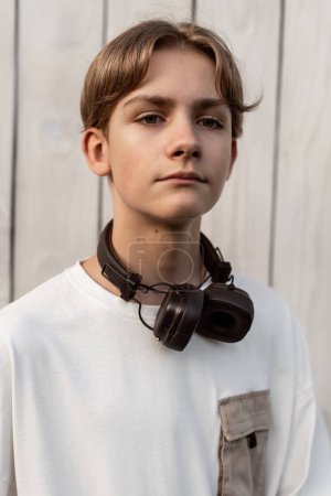 Photo for Portrait of teen boy with headphones outdoor on wooden white background. Child spending free time relaxing. Technology, lifestyle and people concept. - Royalty Free Image