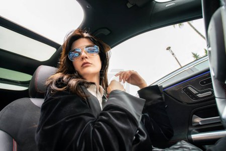 Beautiful black haired sexy girl in dark glasses driving a car. Wide angle. Spectacular attractive woman.