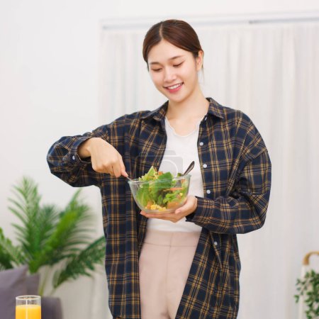Téléchargez les photos : Lifestyle in living room concept, Young Asian woman standing to mixing vegetable salad in bowl. - en image libre de droit