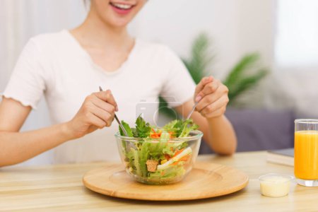 Téléchargez les photos : Style de vie dans le concept de salon, Jeune femme asiatique mélangeant salade de légumes dans un bol pour le petit déjeuner. - en image libre de droit