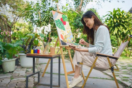 Téléchargez les photos : Concept d'artiste, l'artiste féminine utilise le pinceau pour mélanger la couleur sur la palette pour la peinture sur toile dans le jardin. - en image libre de droit