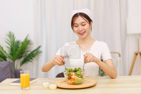 Téléchargez les photos : Style de vie dans le concept de salon, Jeune femme asiatique mélangeant salade de légumes dans un bol pour le petit déjeuner. - en image libre de droit