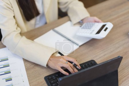 Téléchargez les photos : Concept de secrétaire, secrétaire féminine utilisant une calculatrice pour calculer les dépenses et dactylographier les données sur tablette. - en image libre de droit