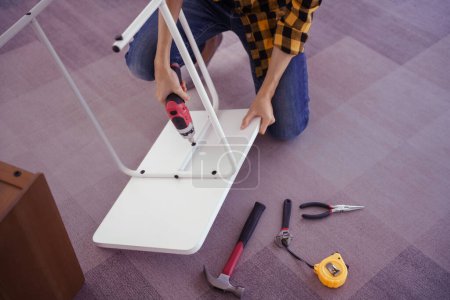 Téléchargez les photos : Les femmes utilisent un tournevis électrique pour visser l'installation et assembler les meubles de table pour la maison neuve. - en image libre de droit