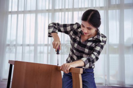 Téléchargez les photos : Femmes utilisant un tournevis pour visser l'installation et assembler une nouvelle chaise tout en faisant des meubles à la maison. - en image libre de droit