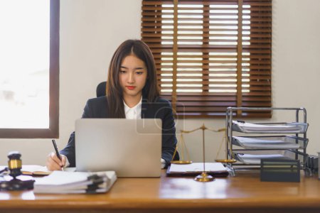 Photo for Legal and justice concept, Young female lawyer reading contract on laptop and writing in notebook. - Royalty Free Image