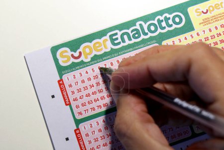 Téléchargez les photos : L'homme joue des numéros sur une carte SuperEnalotto, un jeu de jeu numérique italien avec totalisateurs et prix de SISAL. Photo de haute qualité - en image libre de droit