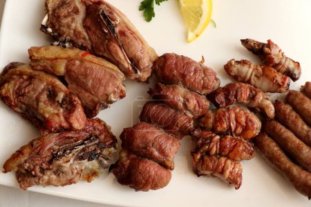 Foto de Mixed roast meat. Lamb, gnummareddi or torcinelli, rolls based on lamb offal, sausage and the famous bombette martinesi, meat rolls stuffed with cheese. Italian food. High quality photo - Imagen libre de derechos