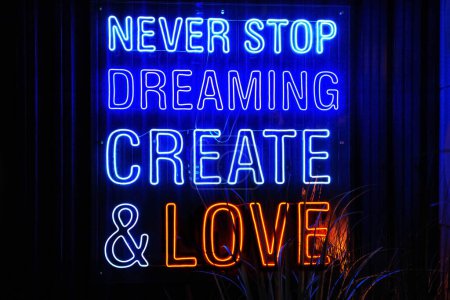 Photo for Blue and Red neon light lettering "Never stop dreaming create and love" in dark, restaurant or cafe. Front view, closeup. - Royalty Free Image