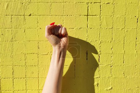 Téléchargez les photos : Femme poing main femelle avec des ongles rouges, poing air punch avec ombre sur fond vert néon jaune. Femmes pouvoir, Fille pouvoir. - en image libre de droit