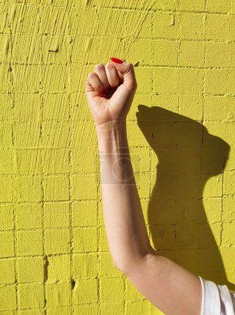 Téléchargez les photos : Femme poing femelle main avec des ongles rouges, poing punch air avec ombre sur fond vert néon jaune. Femmes pouvoir, Fille pouvoir. - en image libre de droit