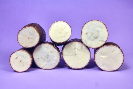 Téléchargez les photos : Racine de manioc biologique fraîche, Manioc Esculenta, yuca sur fond violet, table à main - en image libre de droit
