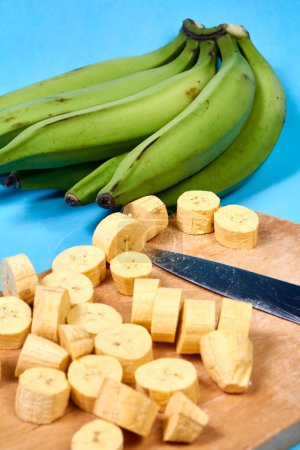 Fresh green banana on blue background, maqueno, barraganete, dominico. hands table knife