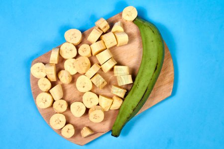 Téléchargez les photos : Banane verte fraîche sur fond bleu, maqueno, barraganete, dominico. couteau de table mains - en image libre de droit