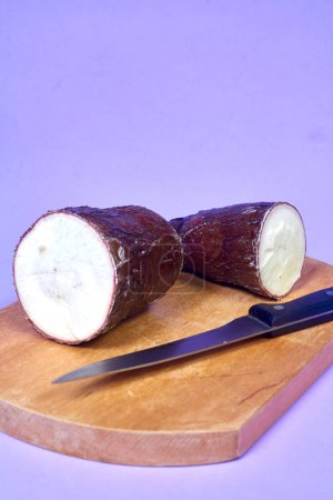 Téléchargez les photos : Racine de manioc biologique fraîche, Manioc Esculenta, yuca sur fond violet, table à main - en image libre de droit