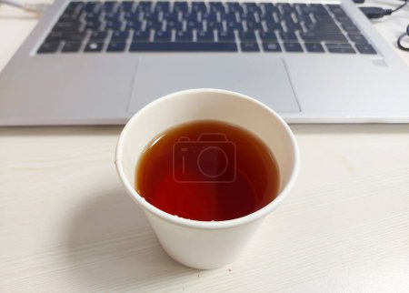 A cup of hot red team kept in front of a laptop in a company.