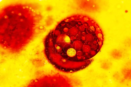 Téléchargez les photos : Grande bulle rouge vif avec de petites bulles flottant à la surface du liquide jaune. Bactéries, molécules, huile. - en image libre de droit