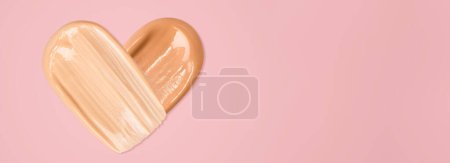 Foto de The foundation is smeared in the shape of a heart on a light pink background. Tone cream - Imagen libre de derechos