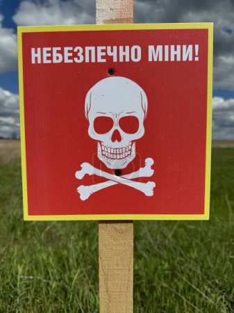 Übersetzung: "Gefährlich, Minen!" Gefahr Minenfeld in der ehemaligen russischen Armee Position. Weißes Totenkopfsymbol auf rotem Schild, das vor der Gefahr warnt. Vorsicht im Minenfeld im ländlichen Raum