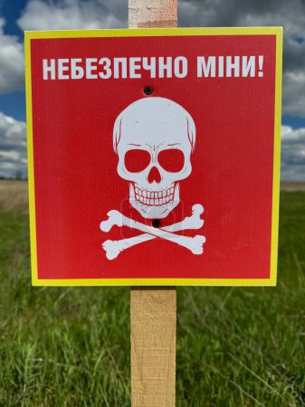 Traducción: "¡Peligroso, minas!" campo de minas de peligro en la antigua posición del ejército ruso. Símbolo blanco de cráneo y huesos cruzados en una señal roja advirtiendo del peligro. Tenga cuidado en el campo de minas en el área rural