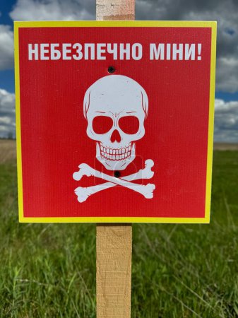 Übersetzung: "Gefährlich, Minen!" Gefahr Minenfeld in der ehemaligen russischen Armee Position. Weißes Totenkopfsymbol auf rotem Schild, das vor der Gefahr warnt. Vorsicht im Minenfeld im ländlichen Raum