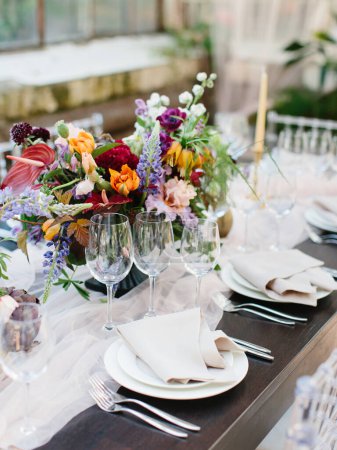 Téléchargez les photos : Décor et service d'une table de banquet de mariage dans un style tropical. Un bouquet coloré d'artichauts, pivoines blanches et roses, tulipes, iris. Verres à vin, bougies, vaisselle, couverts. - en image libre de droit