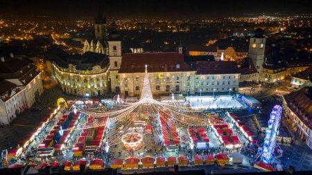 Foto de Fotografía de paisaje del centro de la ciudad de Sibiu con la Feria de Navidad, disparada desde un dron al atardecer con el rayo de la ciudad encendido. Vista de aves sobre paisaje urbano de Sibiu, Rumania. - Imagen libre de derechos