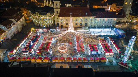 Téléchargez les photos : Photographie de paysage du centre-ville de Sibiu avec la Foire de Noël, prise à partir d'un drone au coucher du soleil avec la foudre de la ville. Vue panoramique sur le paysage urbain de Sibiu, Roumanie. - en image libre de droit