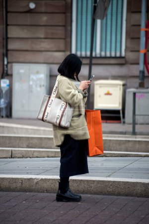 Téléchargez les photos : Strasbourg - France - 31 December 2022 - Portrait of young woman walking in the street with a chloe handbag and smartphone in hands - en image libre de droit