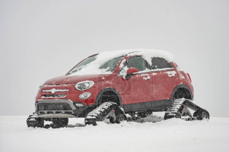 Téléchargez les photos : Voiture avec chenilles sur le sommet d'une montagne dans la neige. Véhicule tout-terrain rouge recouvert de neige sur une route enneigée. - en image libre de droit