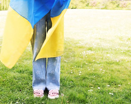 Una chica está de pie en un claro. El niño está envuelto en la bandera de Ucrania. Rezad por Ucrania. Día de la Independencia de Ucrania. Día de la Bandera. Día de la Constitución. Copiar espacio.