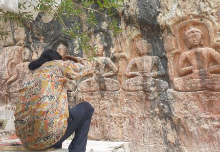 Téléchargez les photos : Back view of a long haired man taking photo of Gyalwa Ringna 5 Dhyani Buddha rock statue while sitting - en image libre de droit