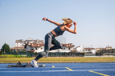 Photo for Woman ready to sprint start in athletics - Sprinter girl in starting blocks ready for the race on the track - Royalty Free Image