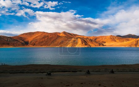 Photo for Ladakh, India - June 26, 2022 : Yellow scooter at Pangong Lake worlds highest saltwater lake in blue stand in stark contrast to the arid mountains surrounding it Vertical or portrait orientation - Royalty Free Image