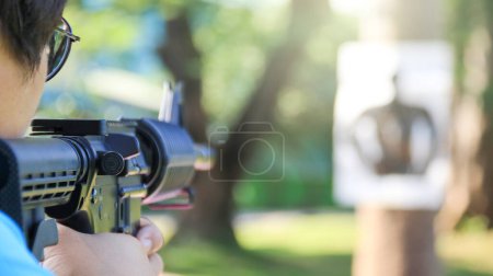 Téléchargez les photos : Pistolet à air doux tenant à la main visant la cible de tir flou dans le champ de tir, foyer doux et sélectif sur le pistolet - en image libre de droit