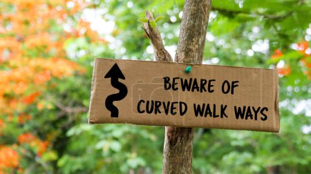 Photo for Brown paper label with drawing of curved direction arrow and the text beware of curved walk ways on tree trunk with blurred background on hiking trails - Royalty Free Image