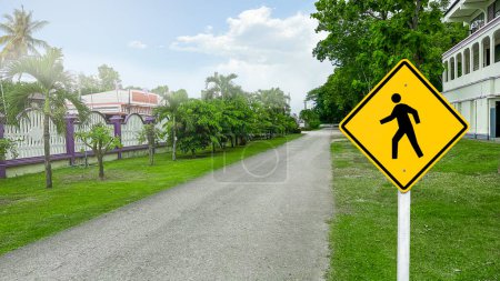 Téléchargez les photos : Panneau piétonnier jaune sur le bord de la route pour avertir les trafics de se méfier des piétons édités avec la lumière du soleil et les arbres flous en arrière-plan - en image libre de droit