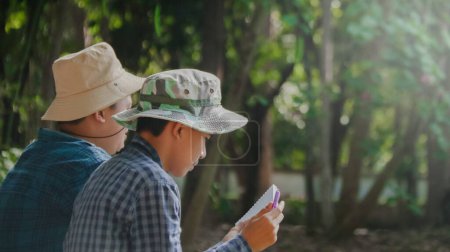 Téléchargez les photos : Les jeunes garçons asiatiques utilisent une jumelle pour surveiller les oiseaux et les animaux dans un parc local, avec un accent doux et sélectif - en image libre de droit