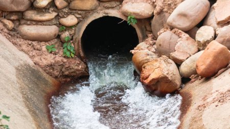 Foto de Agua que fluye de tubería de hormigón en el canal de hormigón que rodea con grandes rocas - Imagen libre de derechos