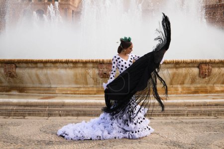 Foto de Bailarina flamenca, morena adolescente y hermosa bailarina típica española baila con un chal negro frente a una fuente en una plaza de Sevilla. Concepto flamenco del patrimonio cultural mundial. - Imagen libre de derechos