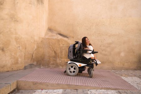 Foto de Hermosa mujer discapacitada joven en una silla de ruedas con movilidad reducida desciende una pendiente accesible para sillas de ruedas. Concepto de eliminación de barreras arquitectónicas - Imagen libre de derechos