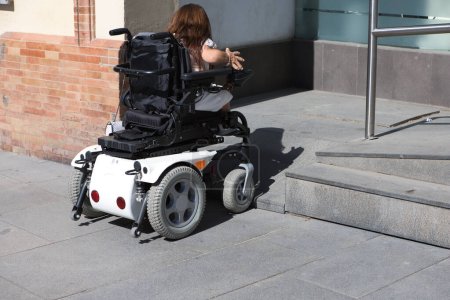 une jeune femme handicapée en fauteuil roulant à mobilité réduite rencontre un obstacle pour accéder à une rampe d'accès pour fauteuil roulant.
